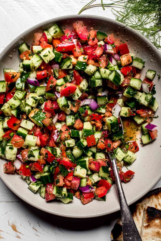 Overhead close up of diced shirazi salad in white bowl with spoon. 