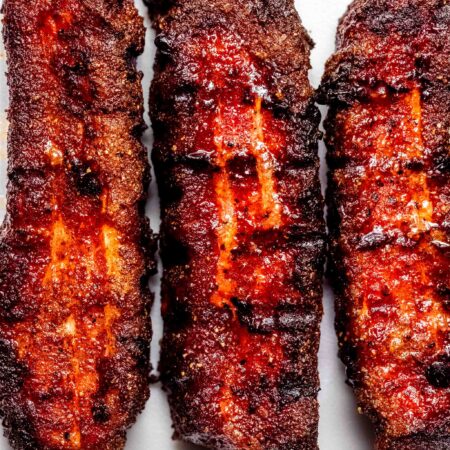 Overhead close up of three smoked pork belly slices with grill marks.