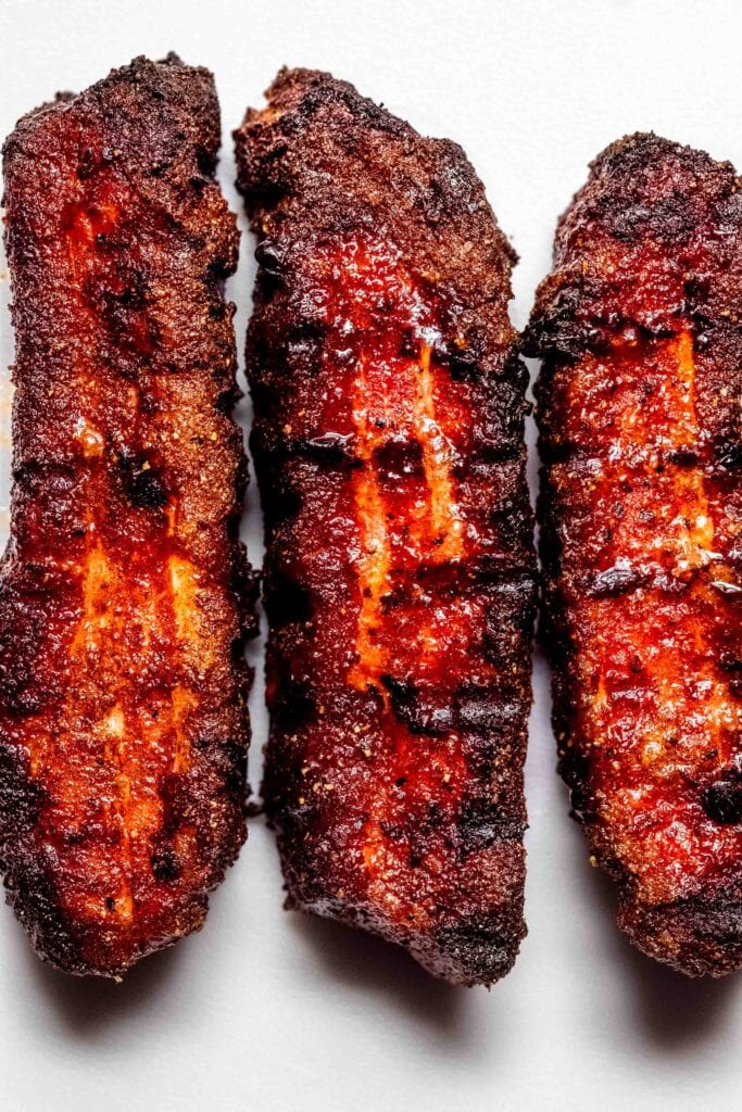 Overhead close up of three smoked pork belly slices with grill marks.