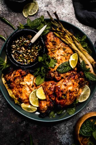 Overhead shot of lemongrass chicken pieces on plate with small bowl of sauce.