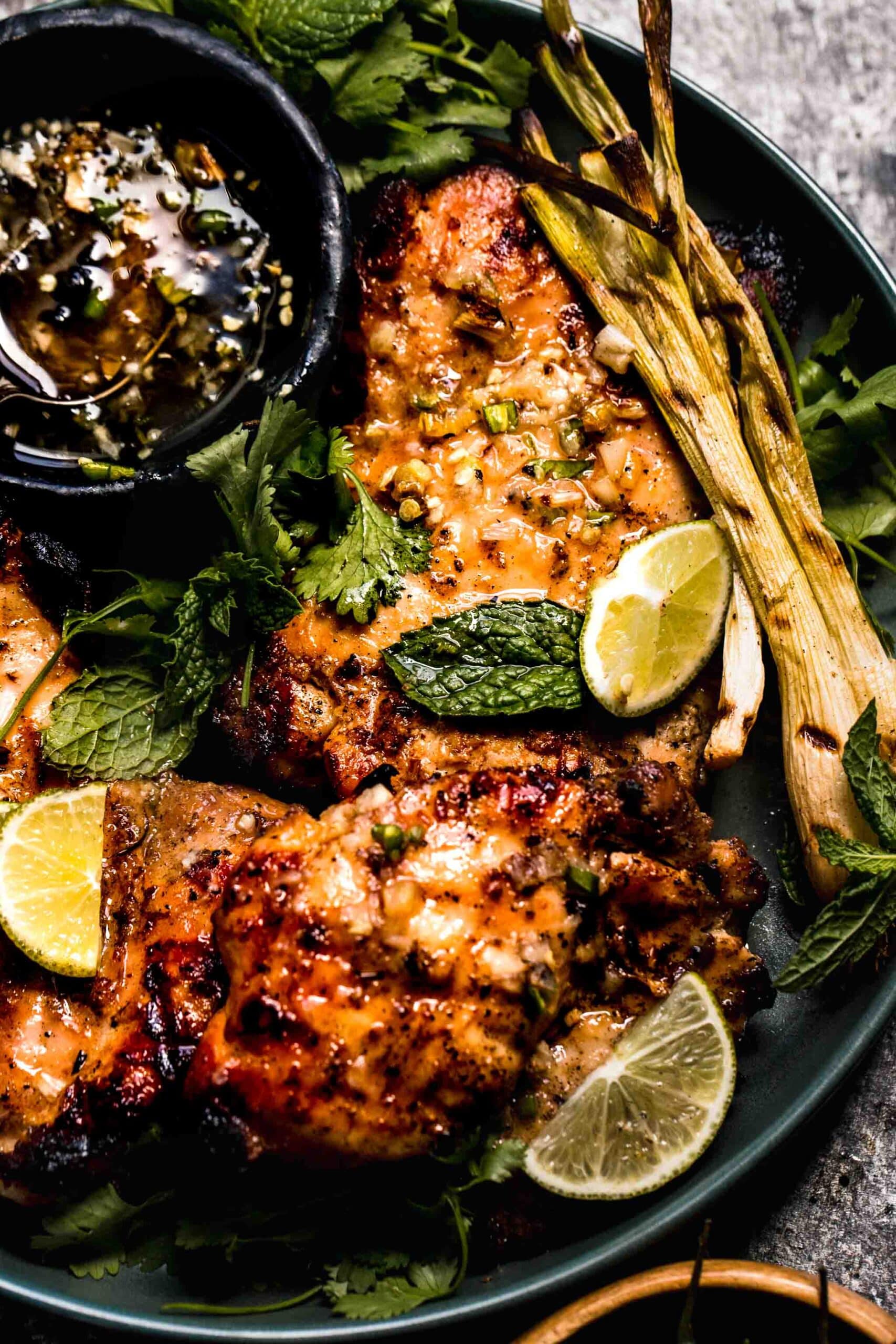 Chicken pieces arranged on plate next to bowl of nuoc cham and scattered with lime wedges.