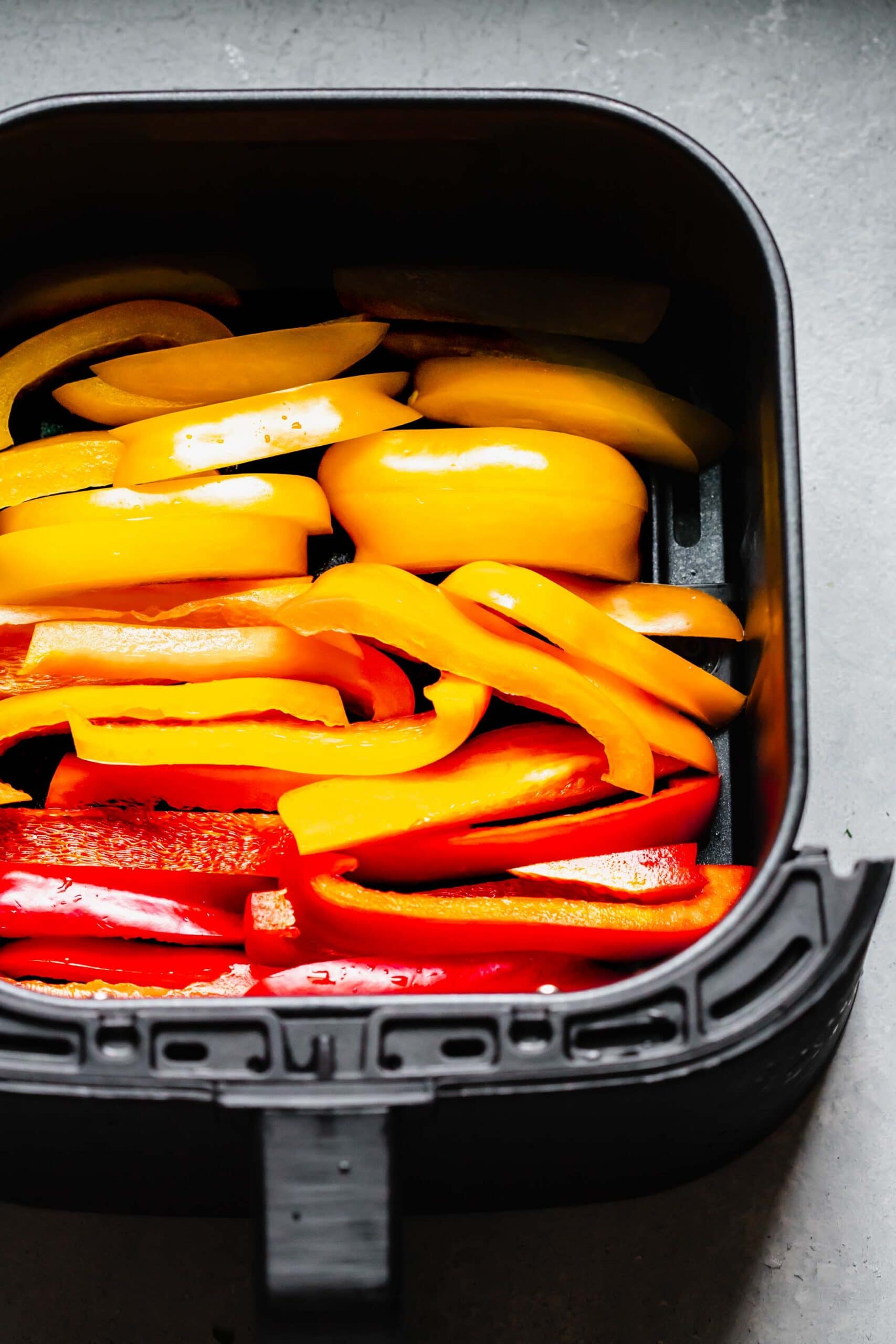 Uncooked peppers in air fryer basket. 
