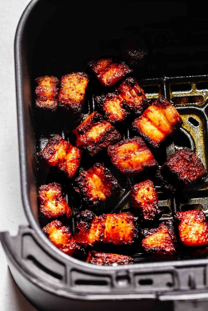 Pieces of pork belly in air fryer basket.