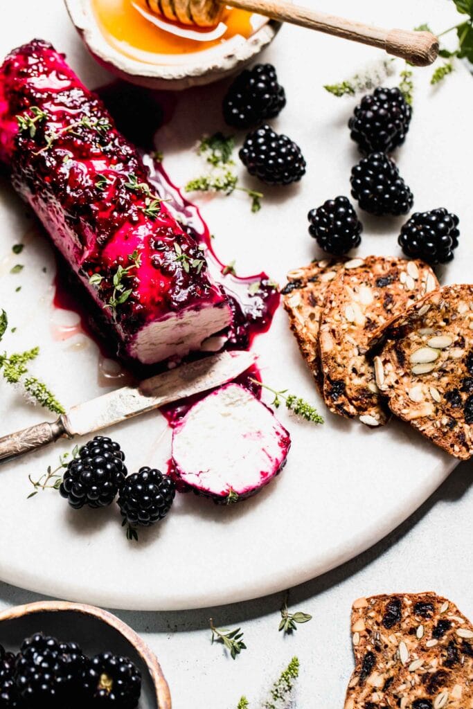 Log of goat cheese on serving platter coated with blackberry mixture and drizzled with honey.