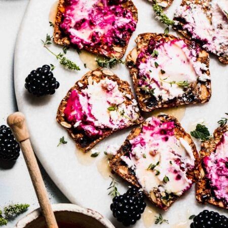 Crackers spread with blackberry goat cheese on serving platter with honey wand and blackberries.