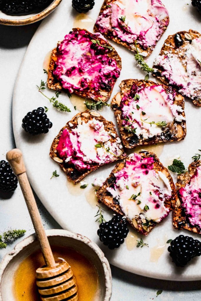 Crackers spread with blackberry goat cheese on serving platter with honey wand and blackberries.
