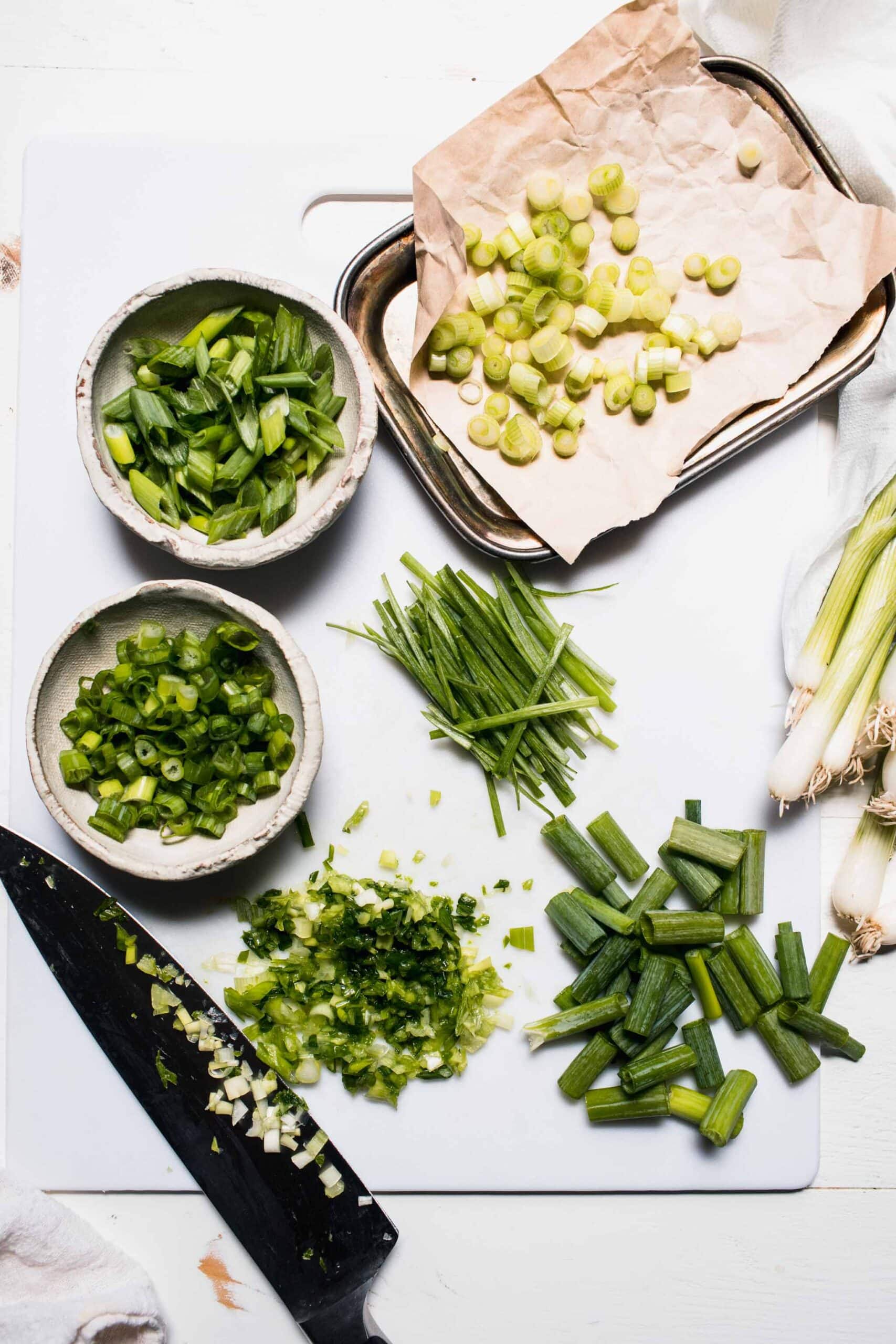 Green onions sliced 4 ways and laid out in small bowls next to knife.