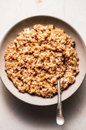 Overhead shot of cooked instant pot farro in white bowl with serving spoon.