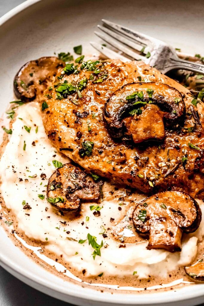 Close up of prepared mushroom chicken breast on plate with mashed potatoes and fork. 