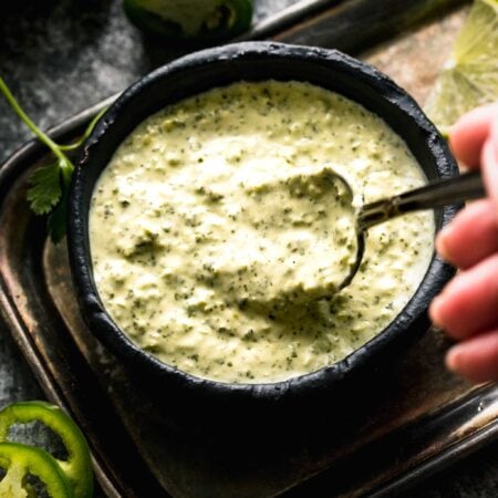 Hand dipping spoon into green sauce.
