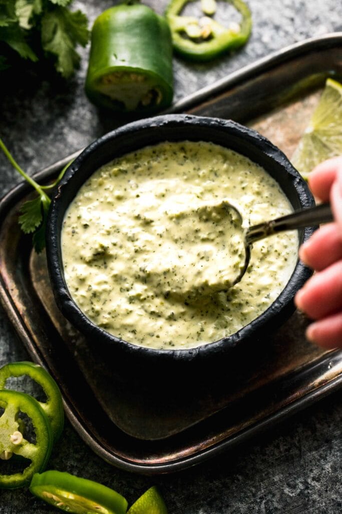 Hand dipping spoon into green sauce.