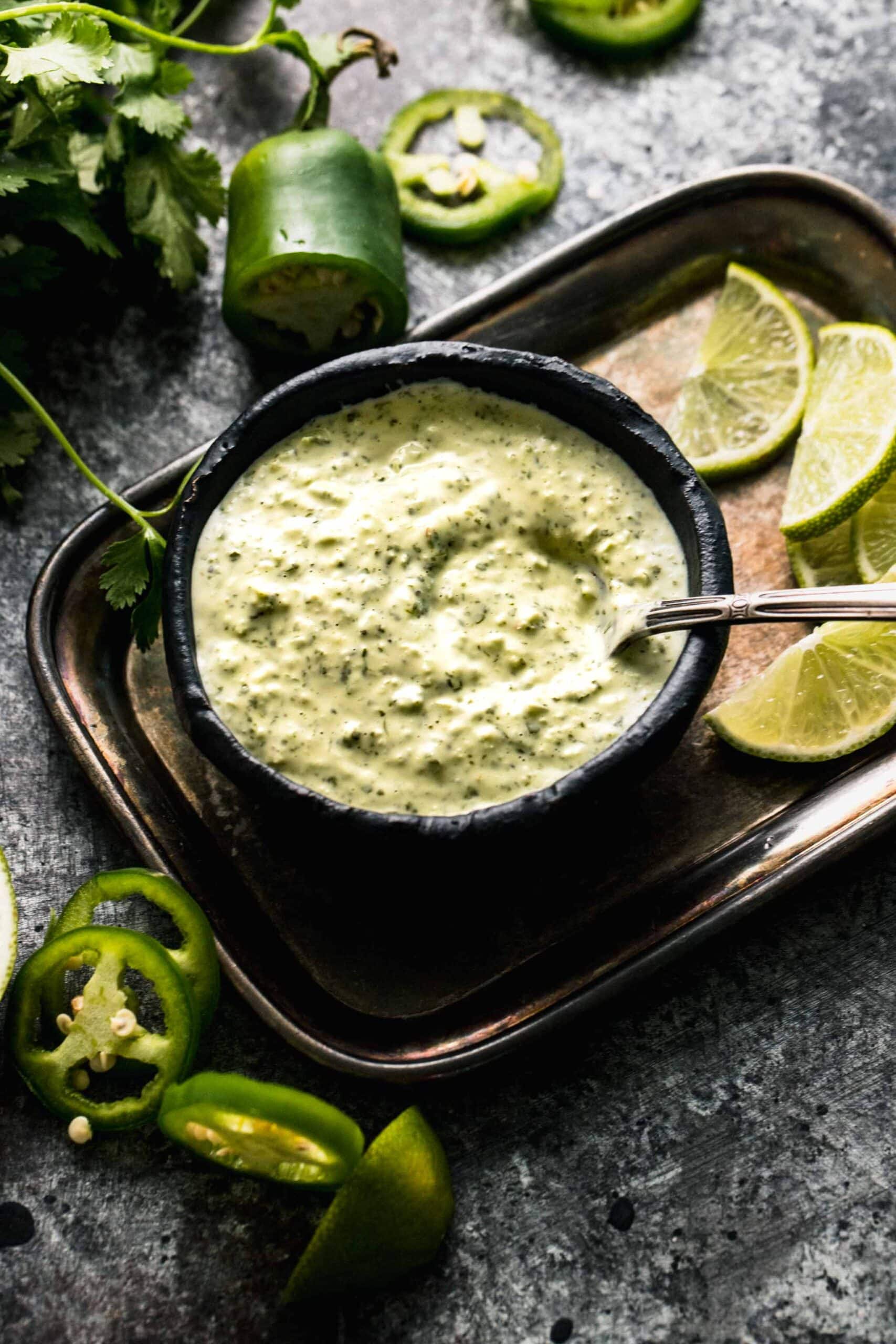 peruvian green sauce in small black bowl surrounded by cilantro leaves.