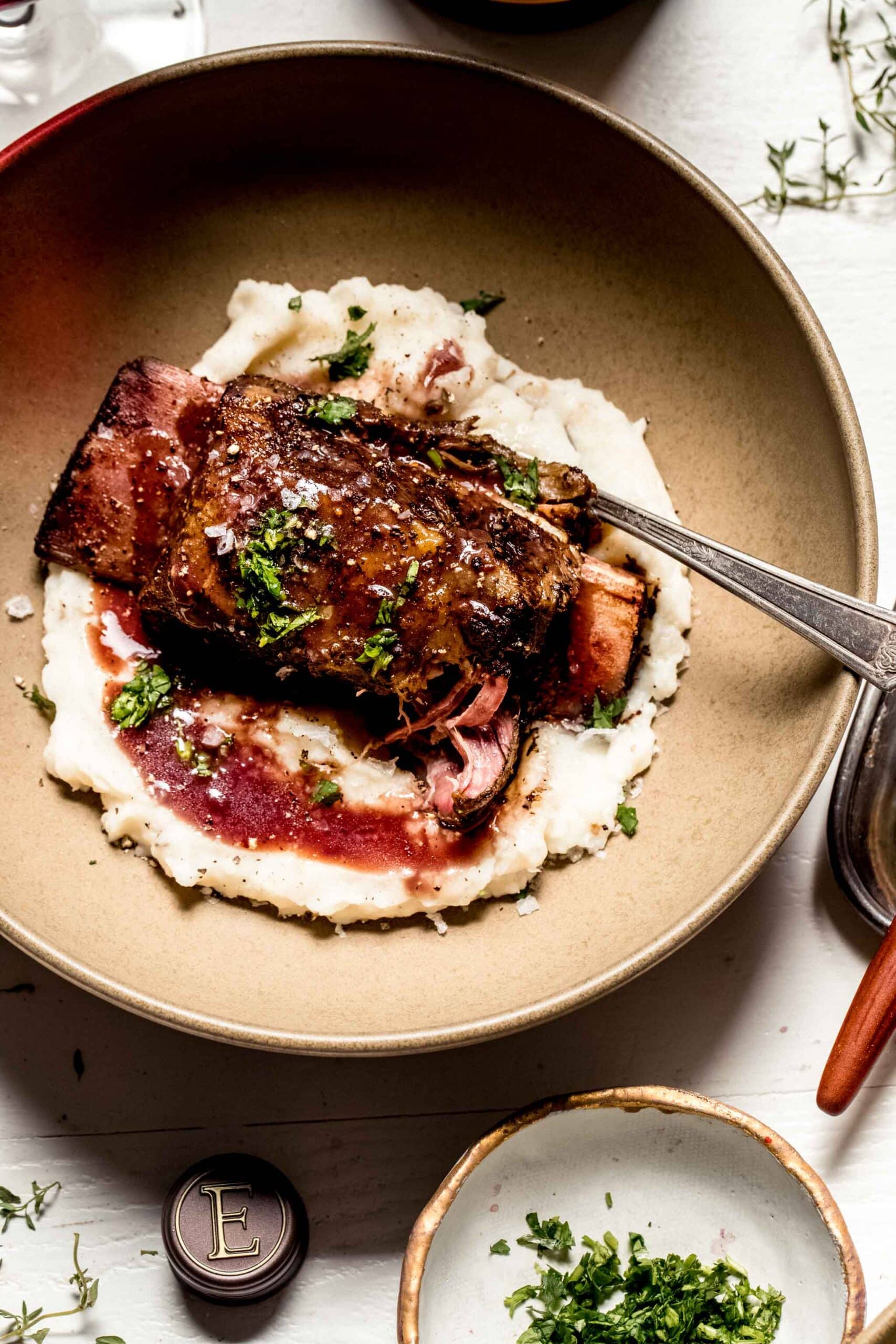 Overhead shot of short rib in brown bowl with mashed potatoes and red wine sauce.