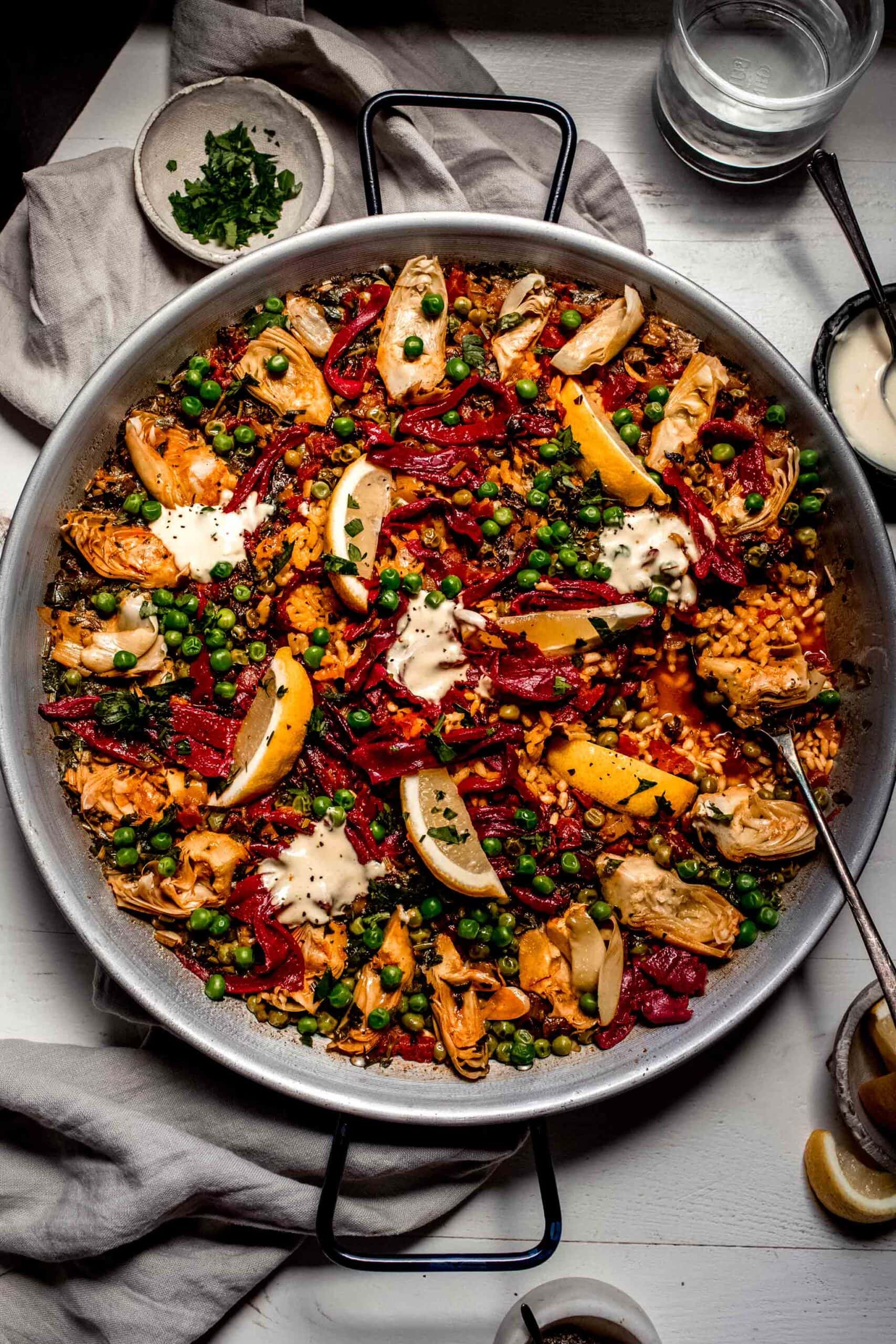 Prepared paella in pan topped with aioli and lemon wedges.