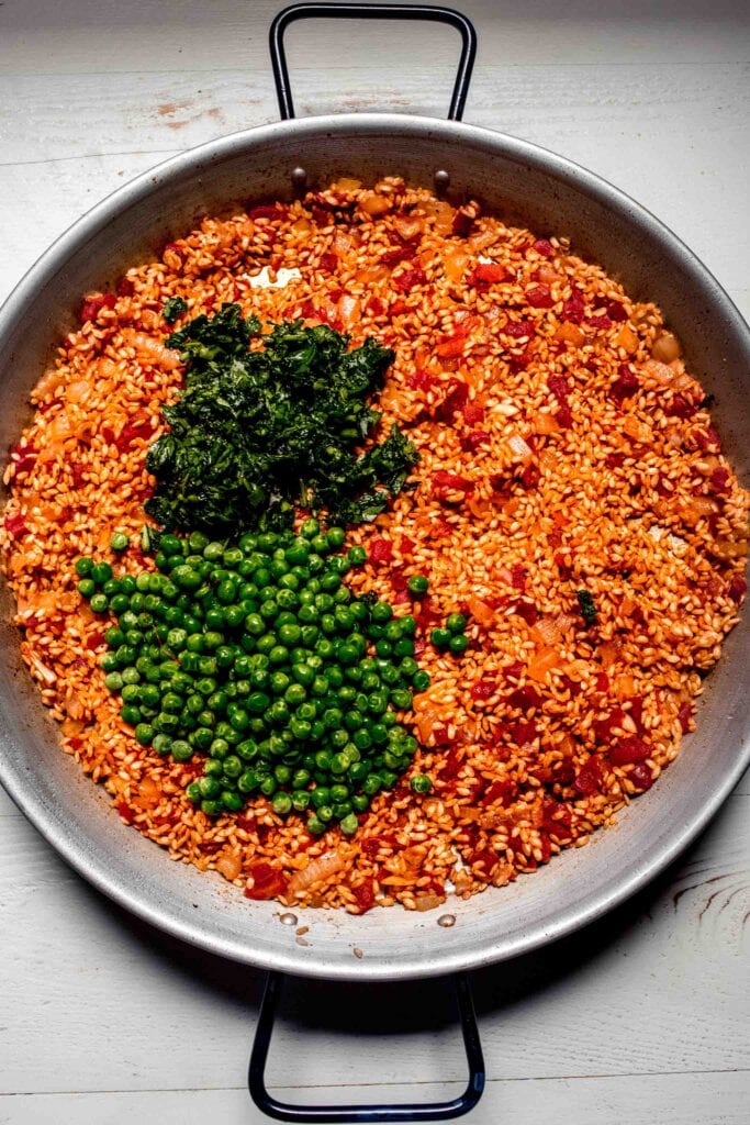 Peas and herbs on top of rice blend in paella pan. 