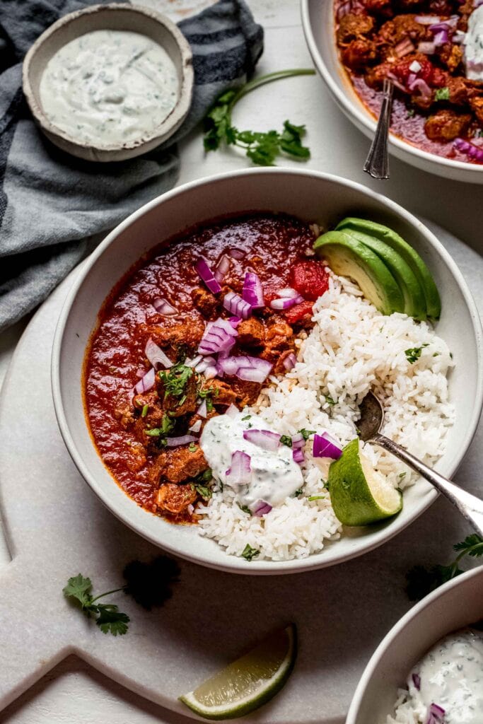Side view of bowl of mexican stew next to bowl of crema. 