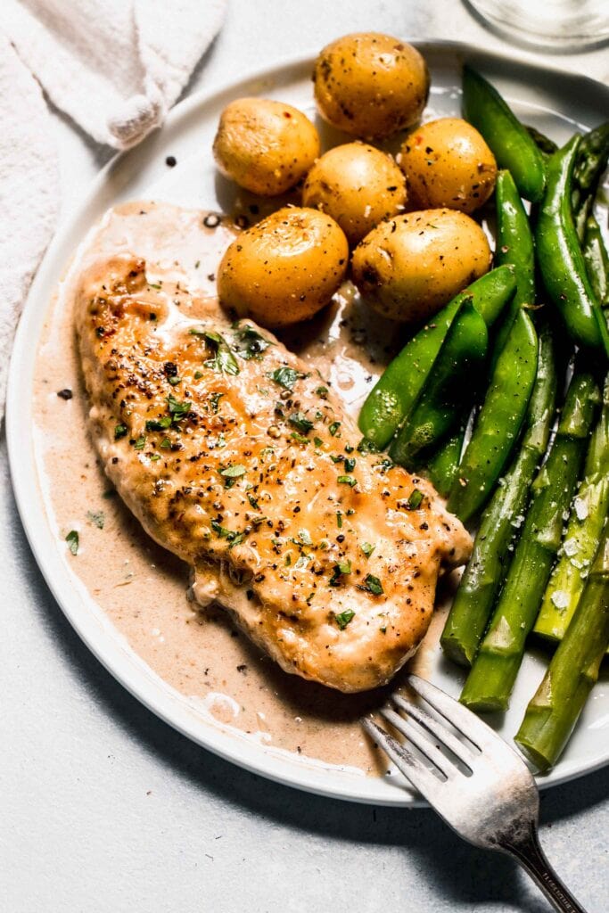Chicken on plate next to potatoes and asparagus.