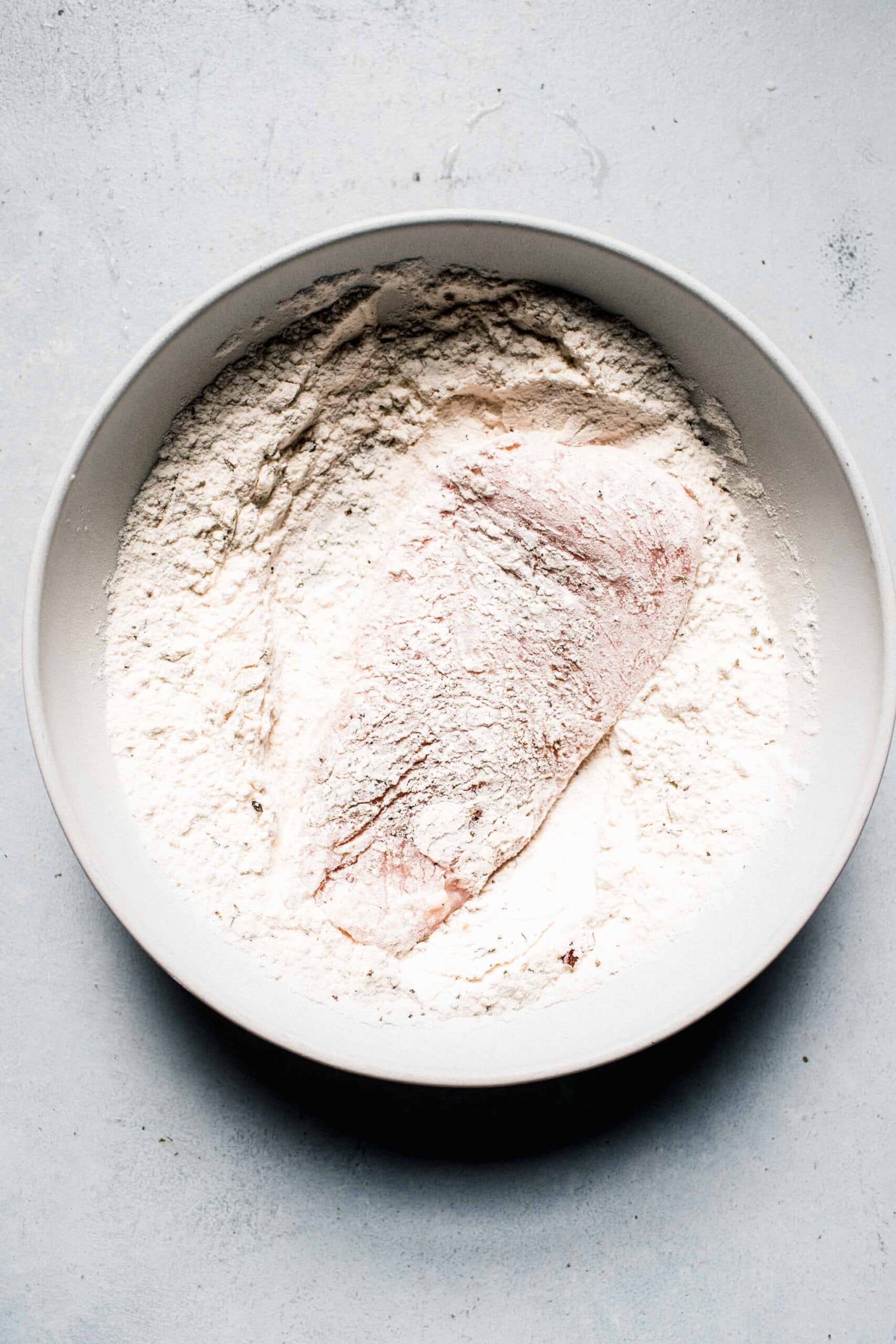 Chicken breast being dredged in flour.