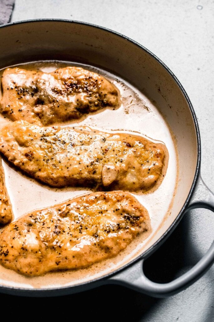Cooked chicken in skillet surrounded by white wine sauce.