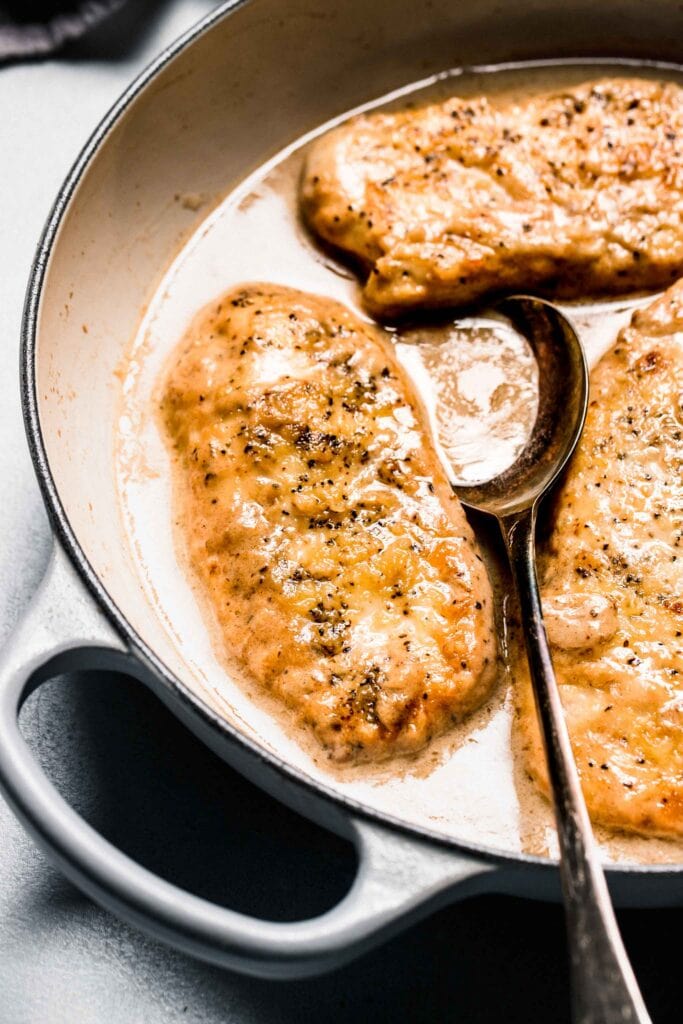 Chicken in white wine sauce in skillet with spoon.