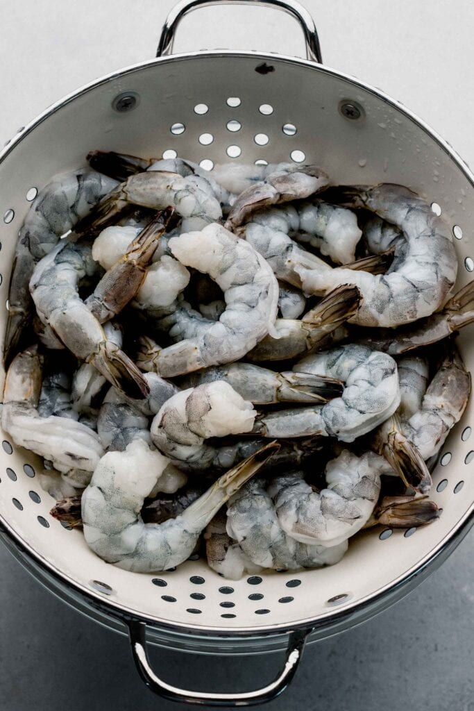 Uncooked shrimp in collander.