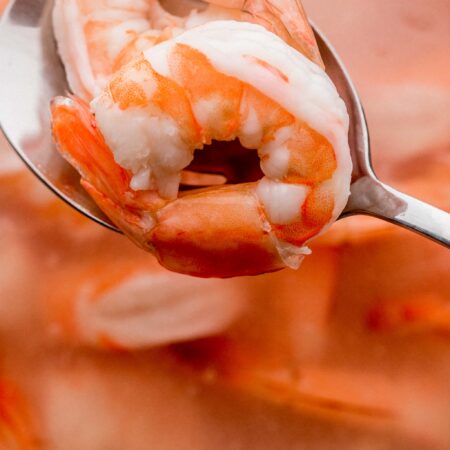 Slotted spoon taking shrimp out of boiling water.