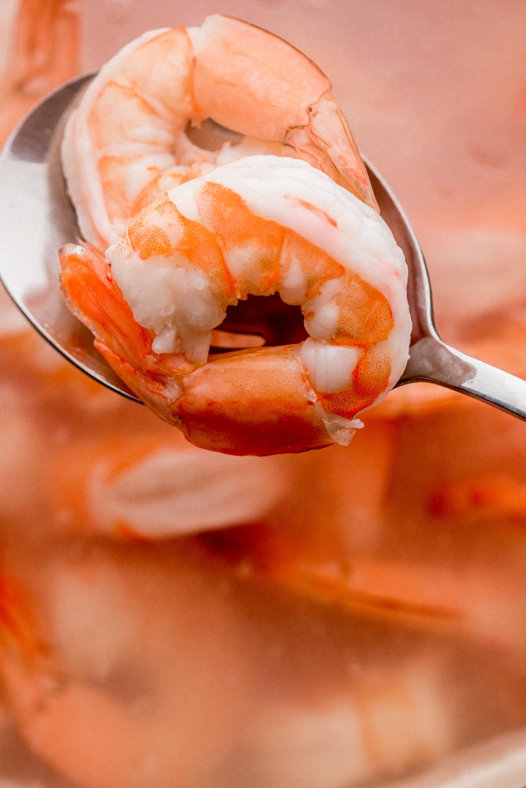 Slotted spoon taking shrimp out of boiling water.