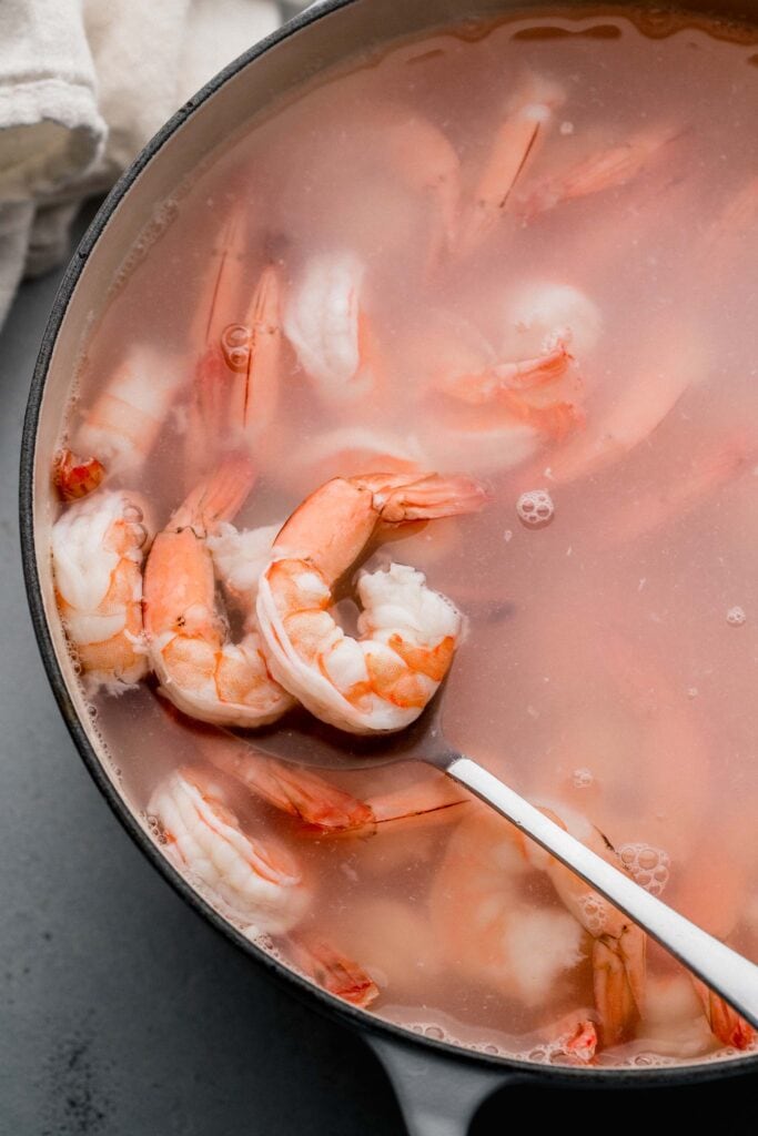 Slotted spoon taking shrimp out of boiling water.