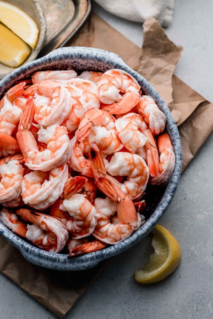 Boiled shrimp in blue bowl next to lemon wedges.