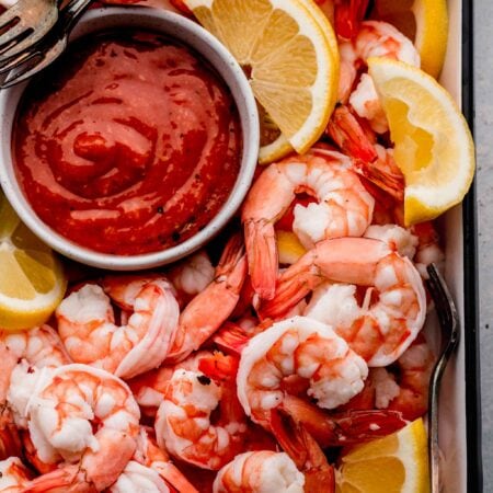 Shrimp, lemon wedges and cocktail sauce arranged in tray with cocktail forks.