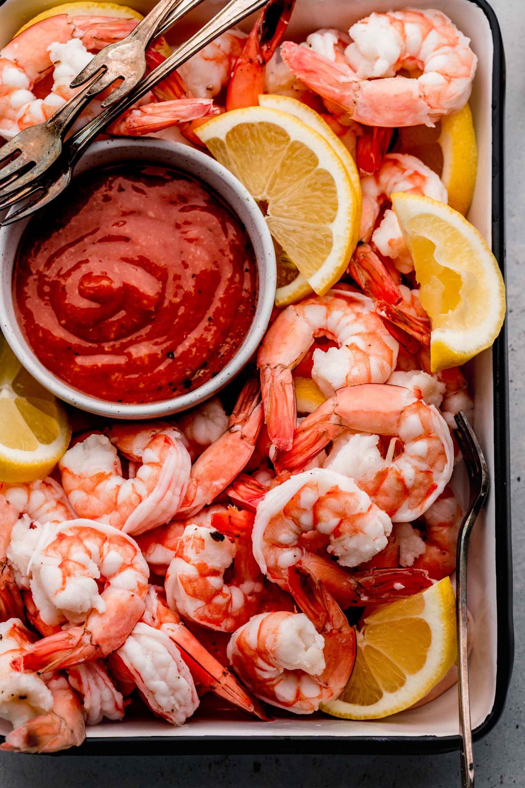 Shrimp, lemon wedges and cocktail sauce arranged in tray with cocktail forks.