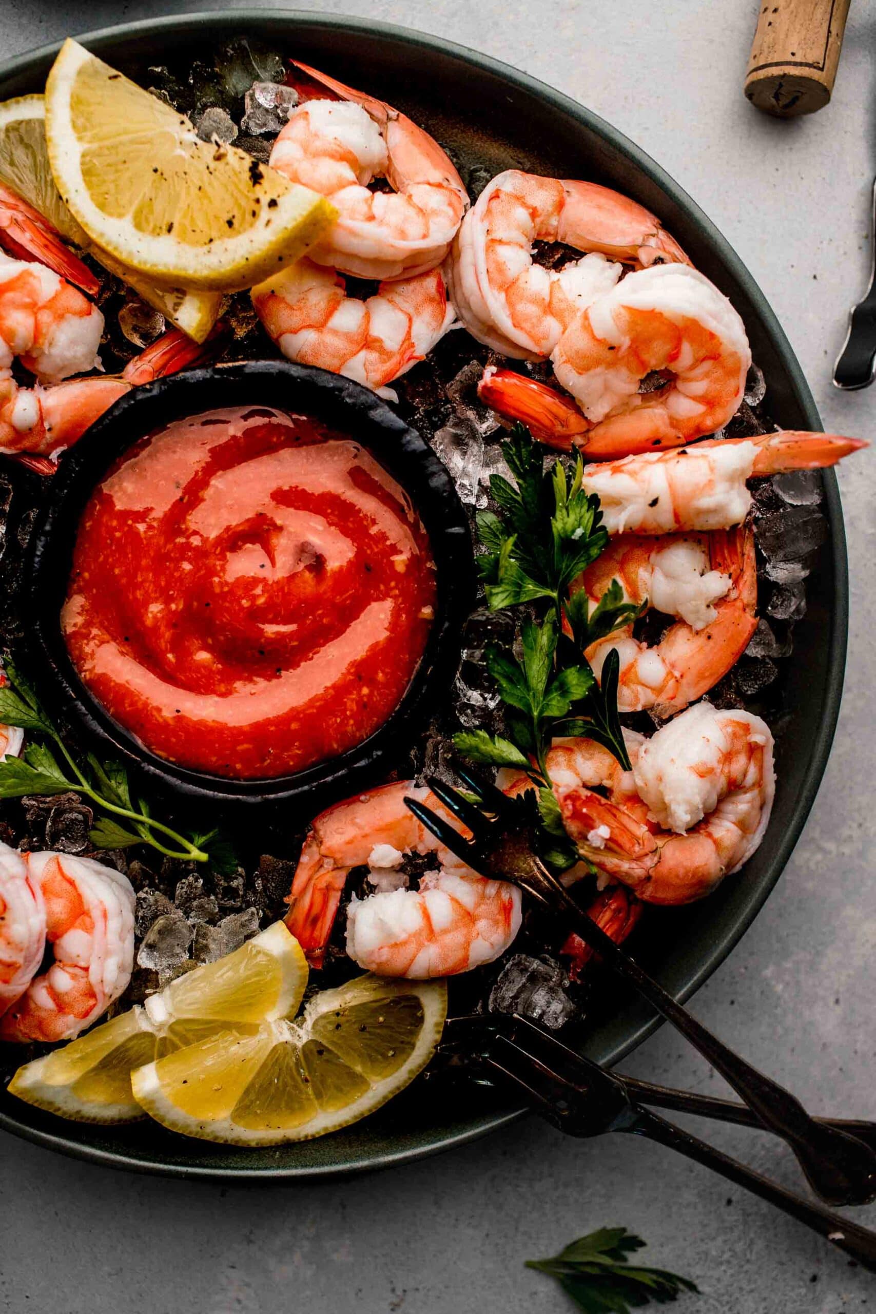 Shrimp arranged in circle on black plate with cocktail sauce in middle.