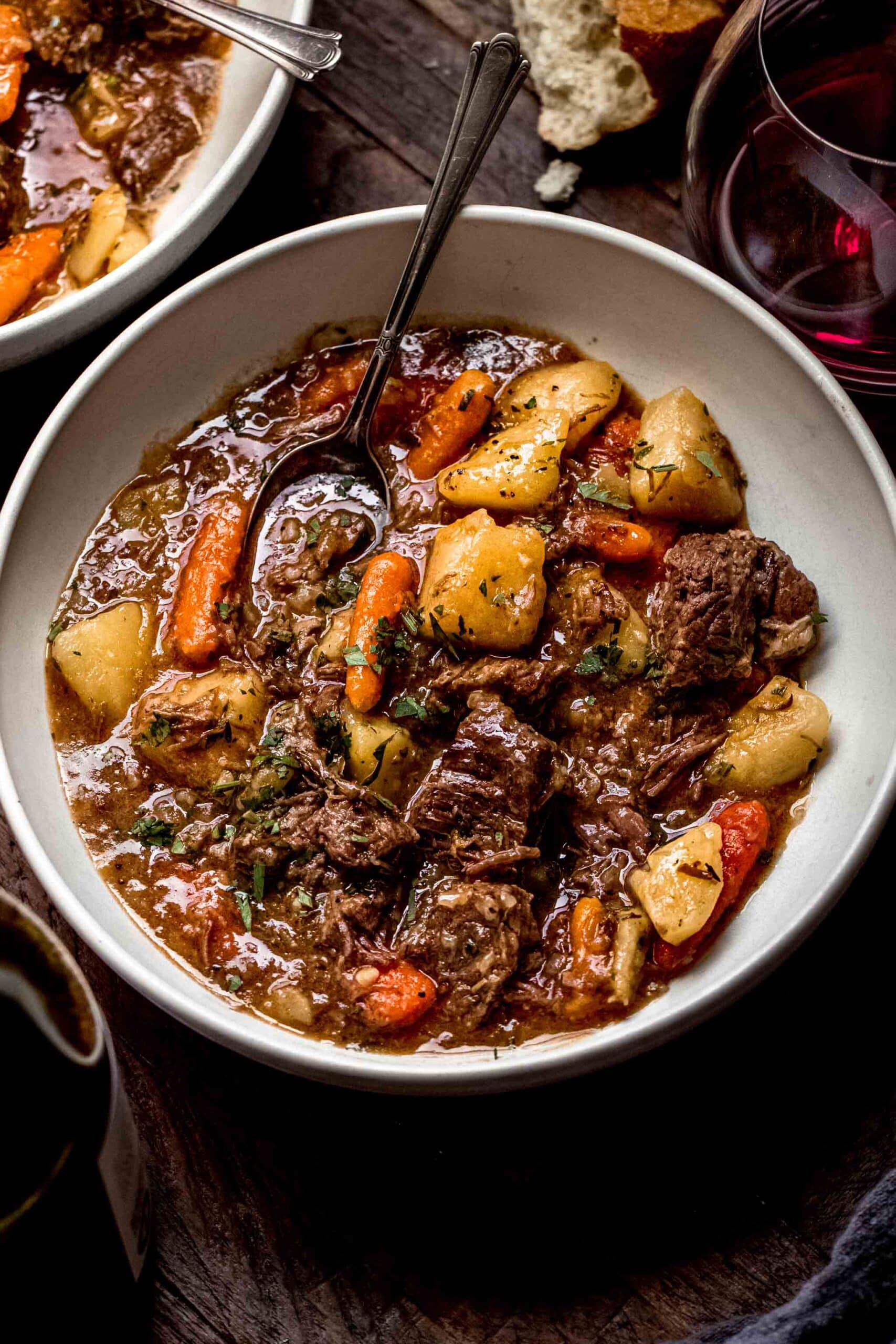 Side view of two bowls of beef stew in white bowl with spoon.