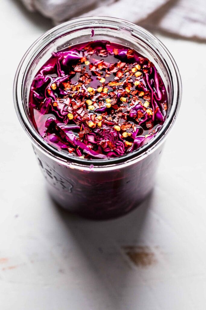 Pickled cabbage in jar sprinkled with pepper flakes.