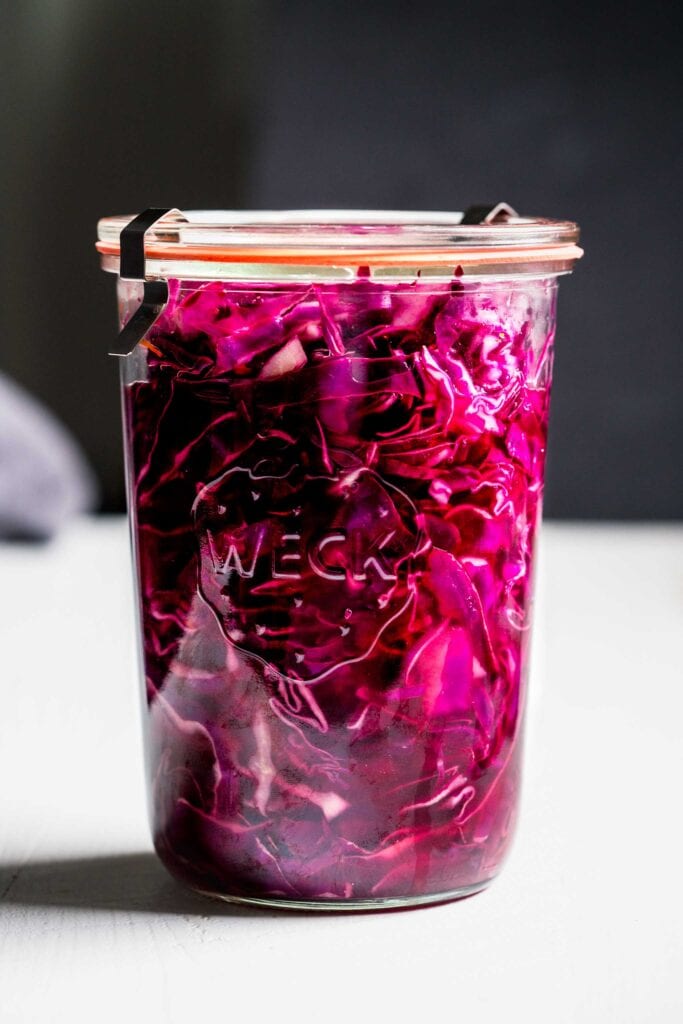 Side view of pickled red cabbage in jar against dark background.