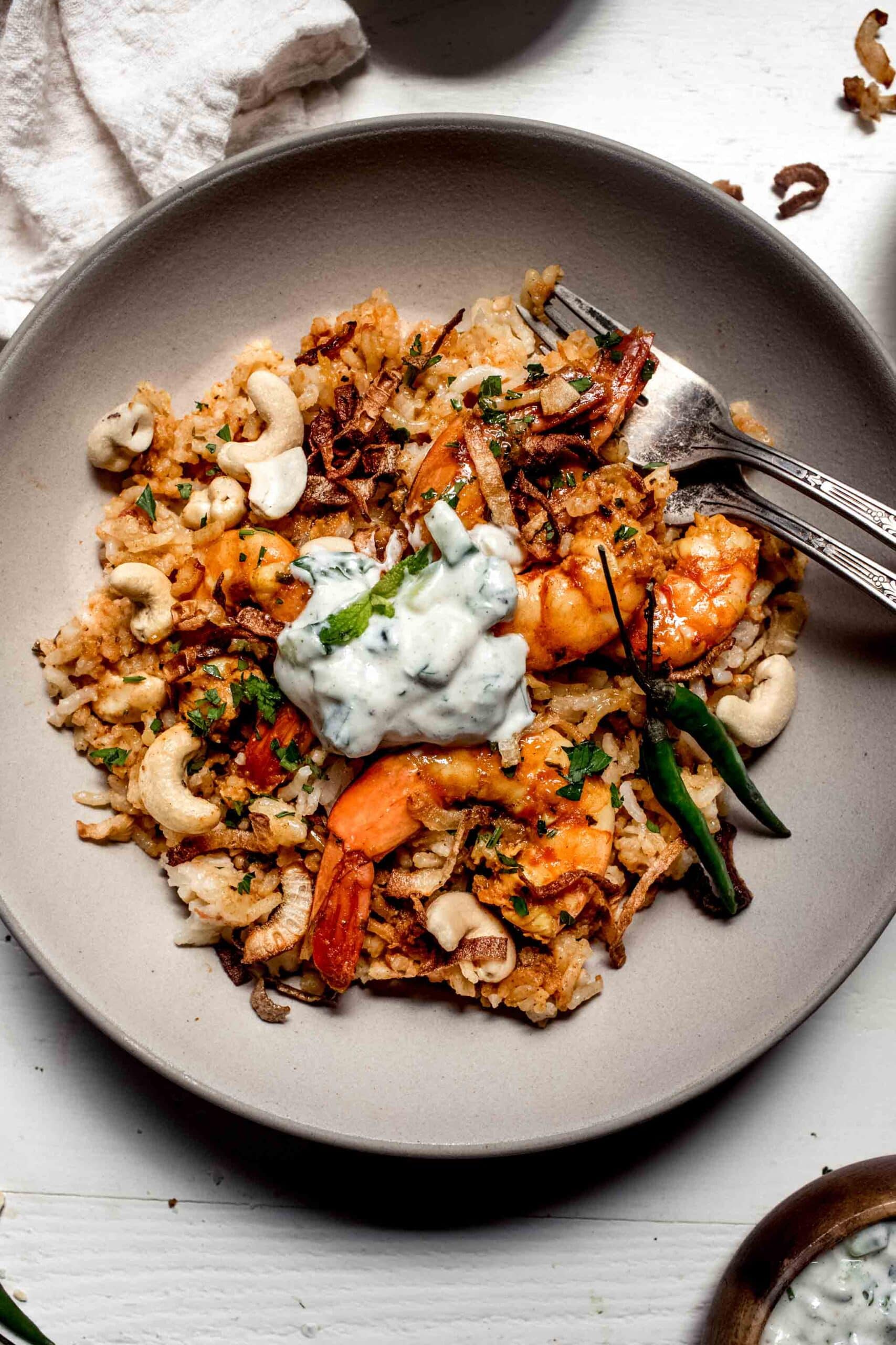 Overhead shot of prawn biryani in serving bowl topped with raita.