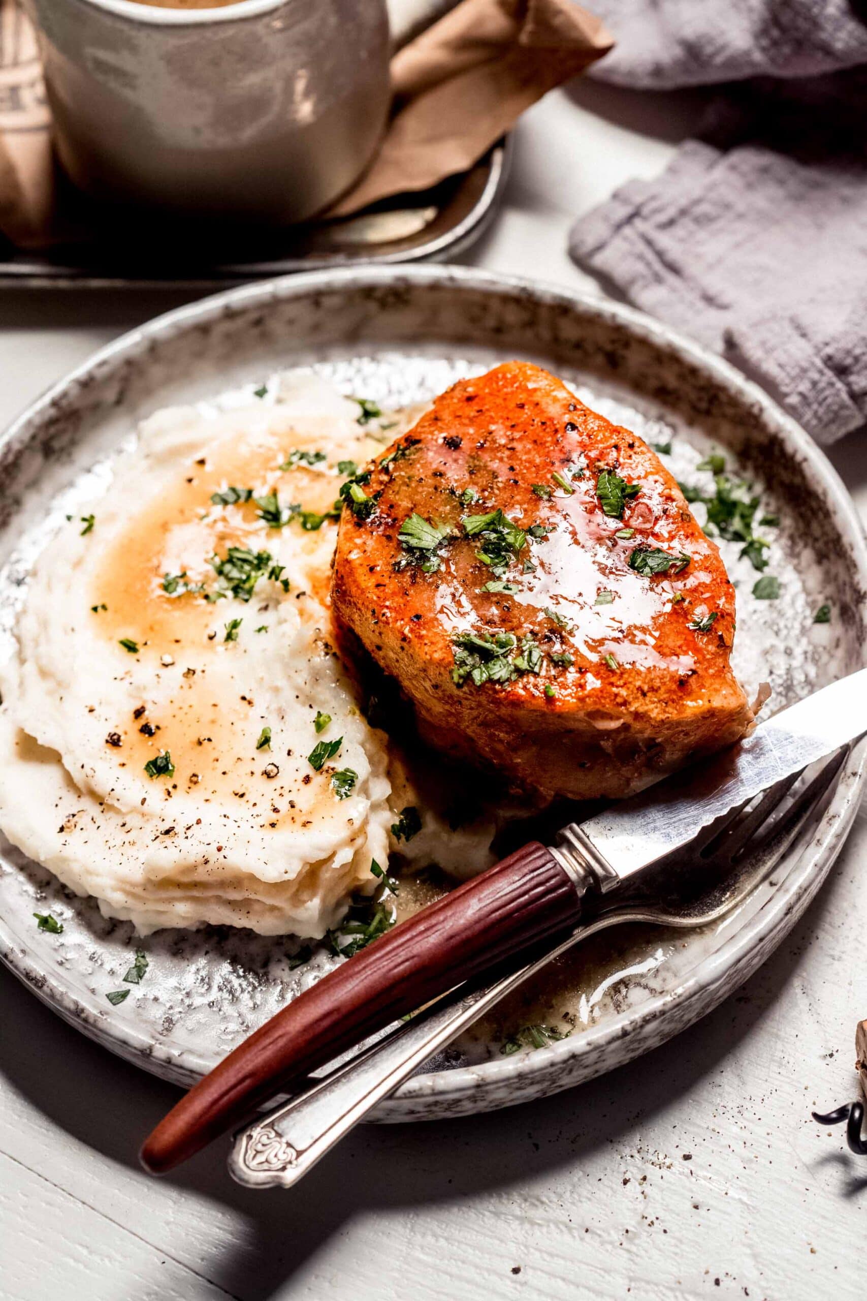 Pork chop on plate next to mashed potatoes and gravy.