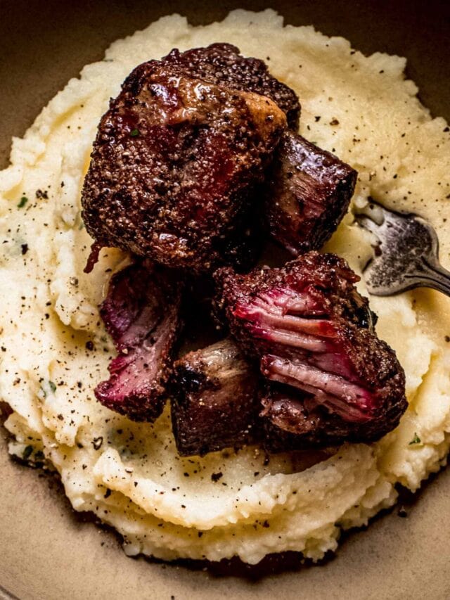 Two smoked beef short ribs in brown bowl on top of mashed potatoes.