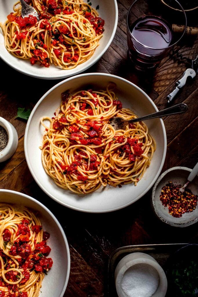 Three bowls of spaghetti with diavolo sauce on wood counter.