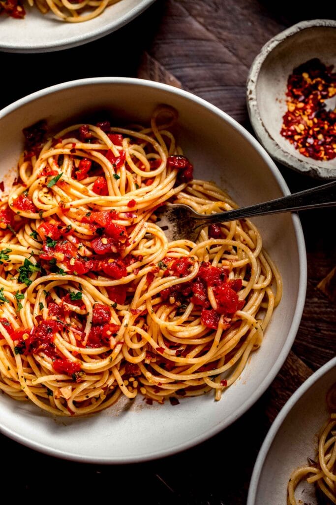 Three bowls of spaghetti with diavolo sauce on wood counter.