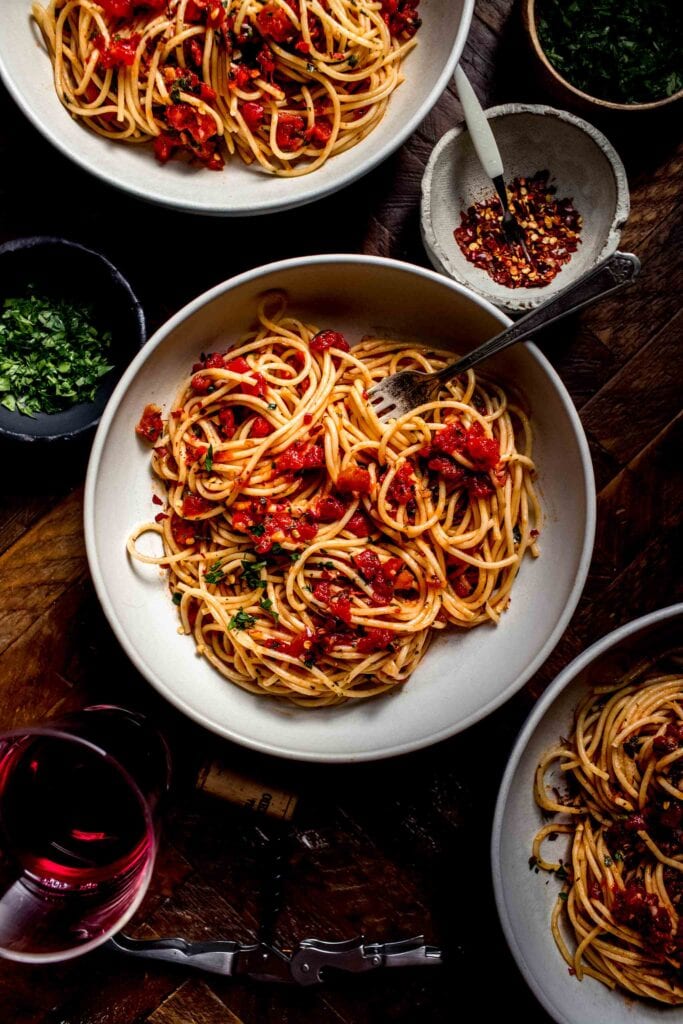 Three bowls of spaghetti with diavolo sauce on wood counter.