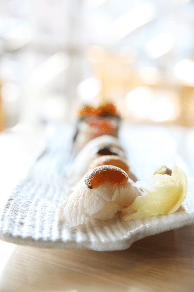 Hamachi sushi on plate next to ginger. 