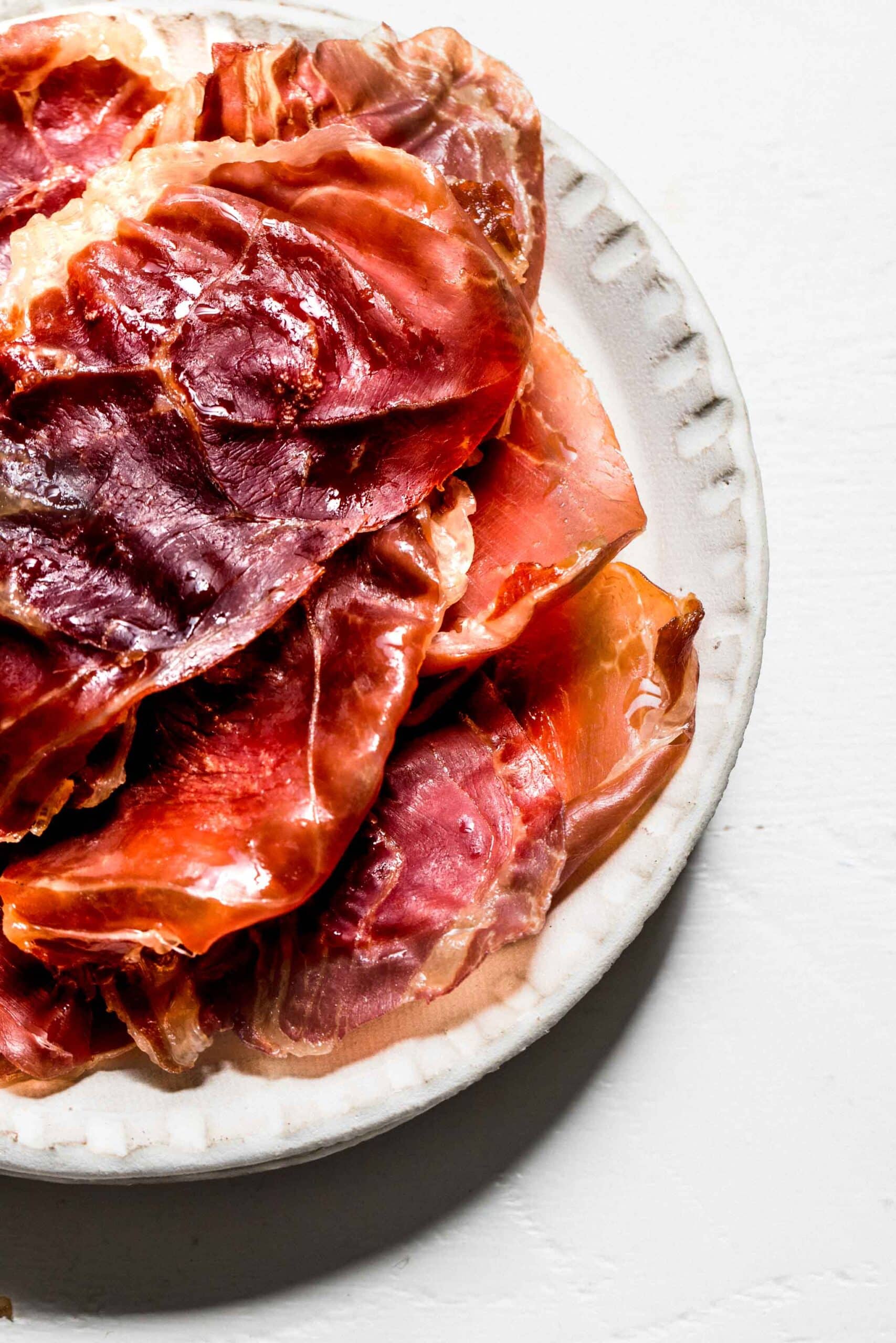 Crispy prosciutto slices stacked on white plate.