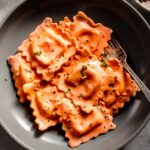 Bowl of lobster with creamy sauce in grey bowl next to glass of wine.