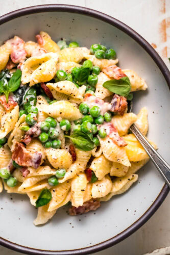 Overhead close up of finished pea and bacon pasta in serving bowl.