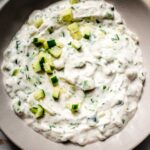Overhead shot of prepared raita sauce in bowl next to pita pieces.