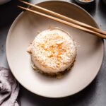 Coconut rice in dome shape in bowl with chopsticks next to rice cooker.