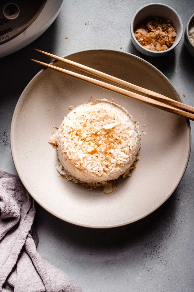 Coconut rice in dome shape in bowl with chopsticks next to rice cooker.