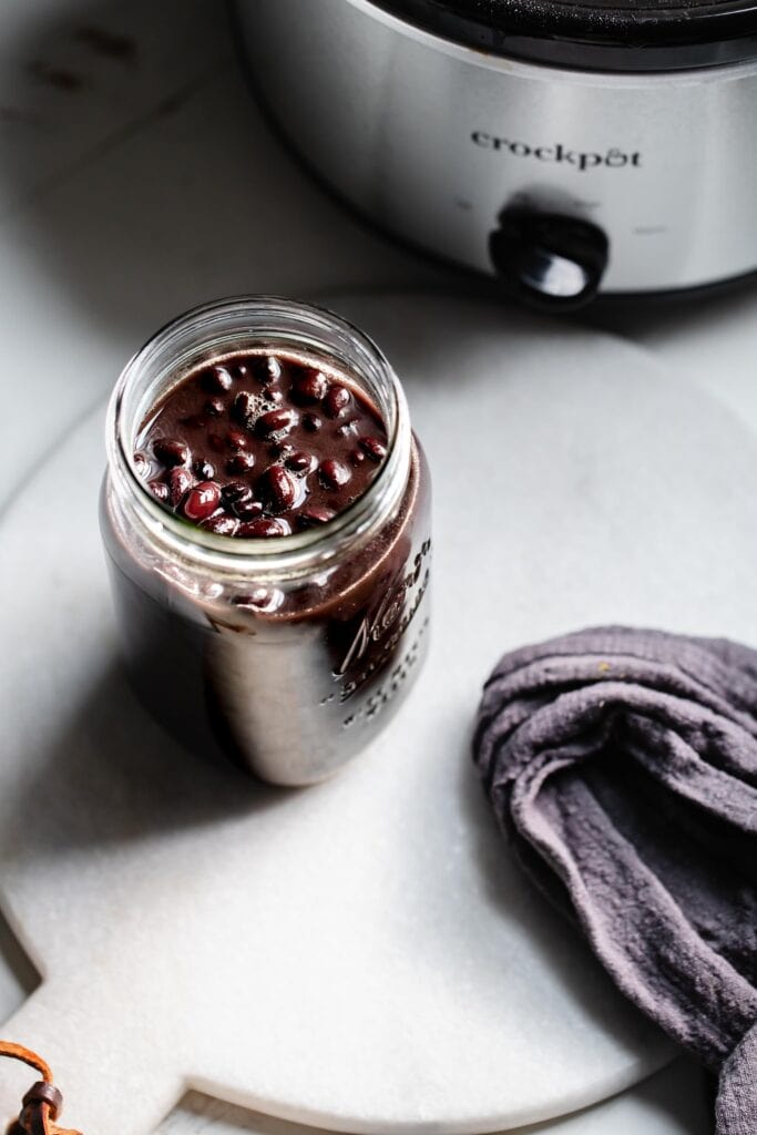 Cooked beans in jar next to slow cooker.