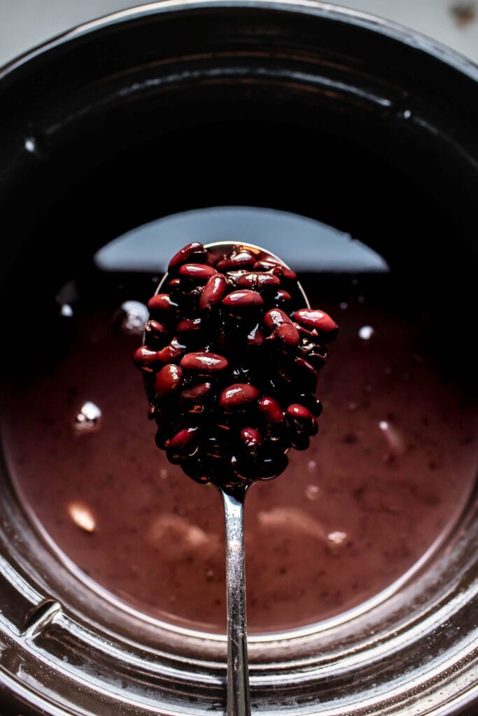 Cooked black beans in spoon over slow cooker.